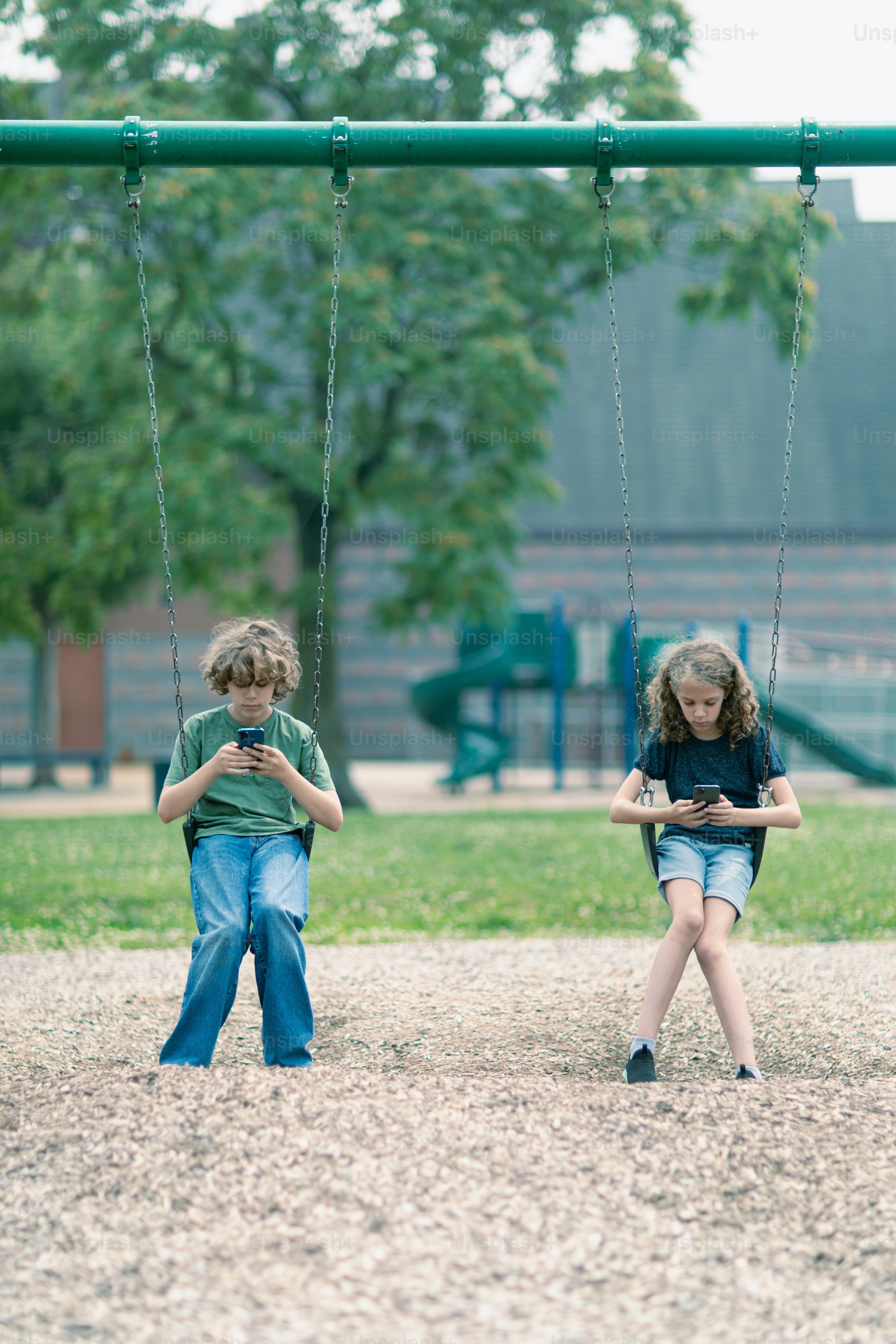 two children playing on a swing set in a park